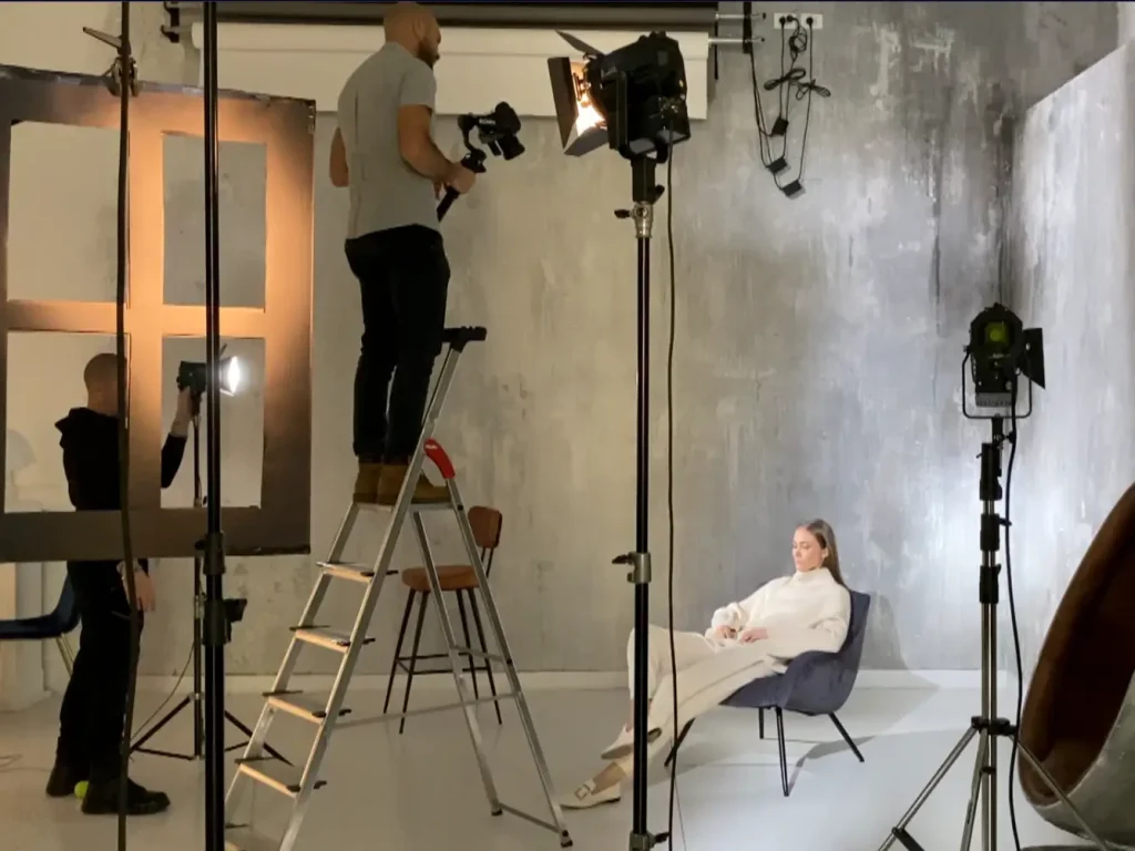 Sessione di scatto in studio con modella su sedia e fotografo su scala.