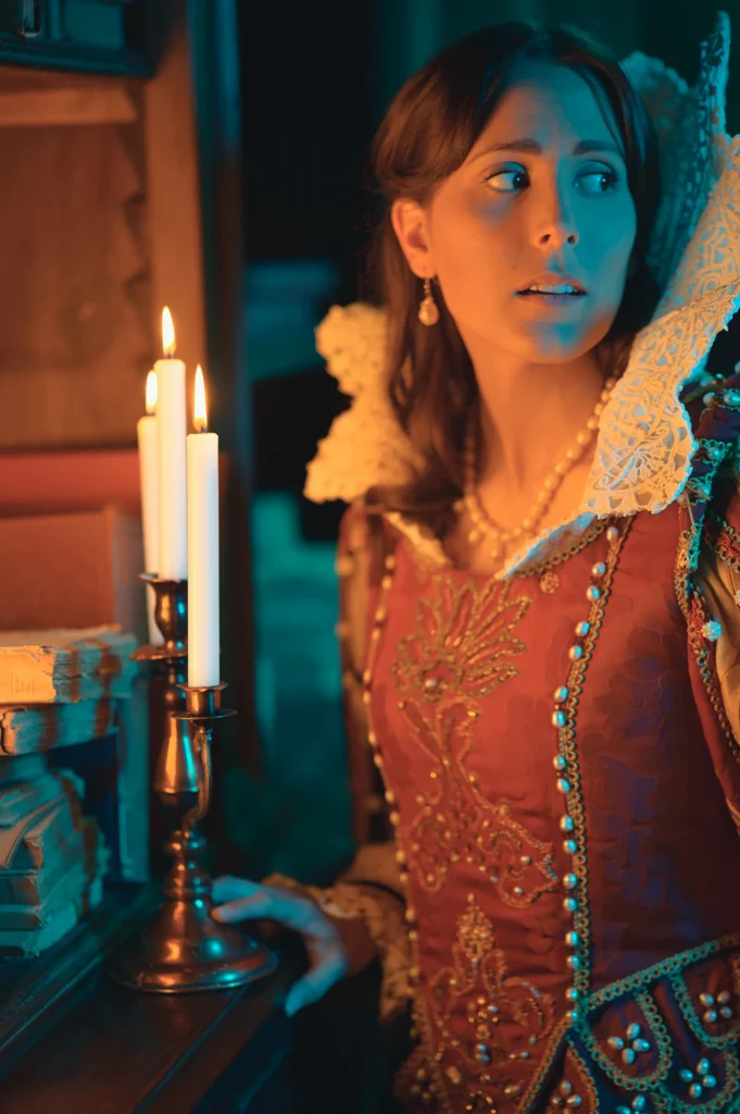 Ragazza vestita da Dama del 1500 con abiti storici in una scena realizzata in una antica biblioteca del 500, che posa per una foto in stile cinematografiche Staged Photography, realizzata da Francesco Francia Fotografo di moda e ritratto. Illuminata da una candela e luci cinematografiche artificiali Nanlite