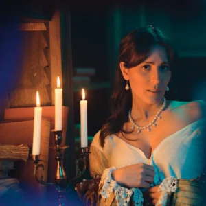 Ragazza vestita da Dama del 1500 con abiti storici in una scena realizzata in una antica biblioteca del 500, che posa mentre si spoglia davanti una figura, per una foto in stile cinematografiche Staged Photography, realizzata da Francesco Francia Fotografo di moda e ritratto. Illuminata da una candela e luci cinematografiche artificiali Nanlite